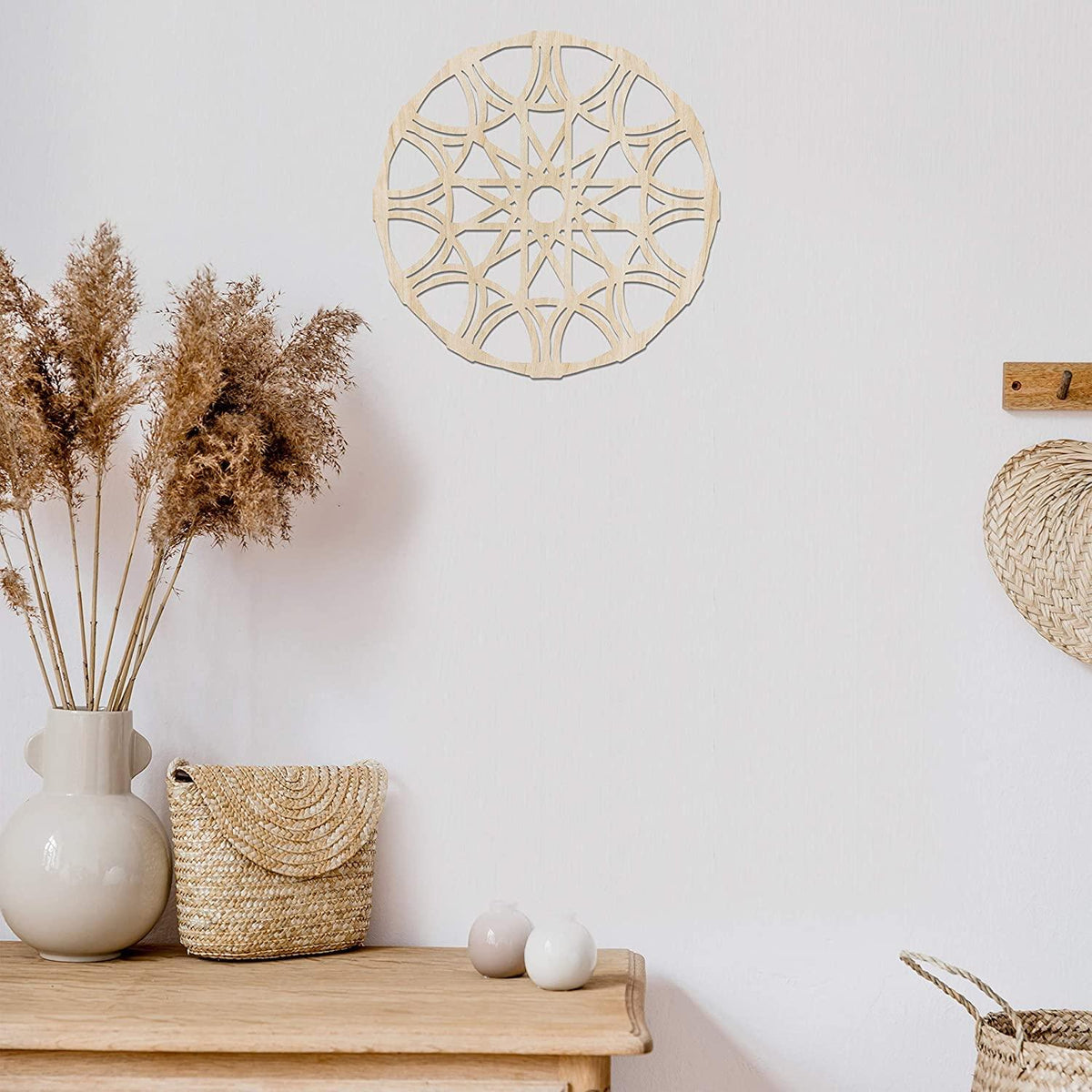 Natural wood mandala wall art hung on a white wall above a console table with dried grasses